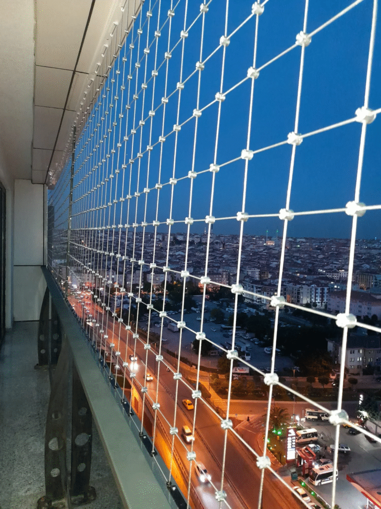 Yüksek kat balkonunda metal bağlantılarla çevre yüzeylere sabitlenmiş kare çelik ağ